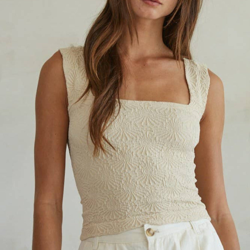Woman wearing a beige lace top against a plain background
