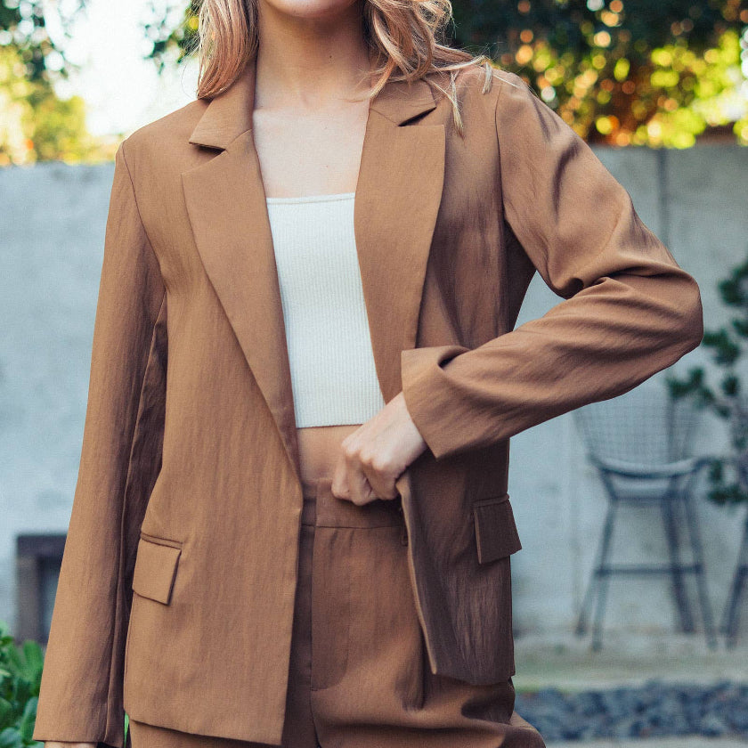 Woman wearing a brown suit with a white top outdoors.