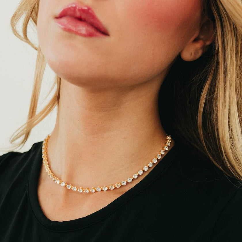 Close-up of a person wearing a gold necklace with a plain background