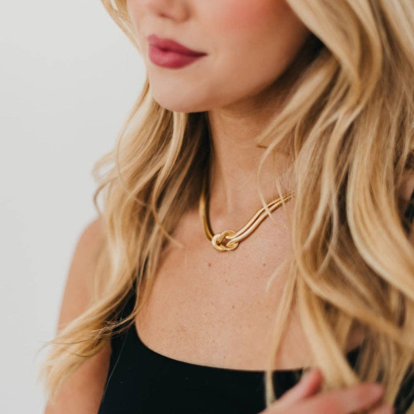 Close-up of a person wearing a gold necklace with a plain background