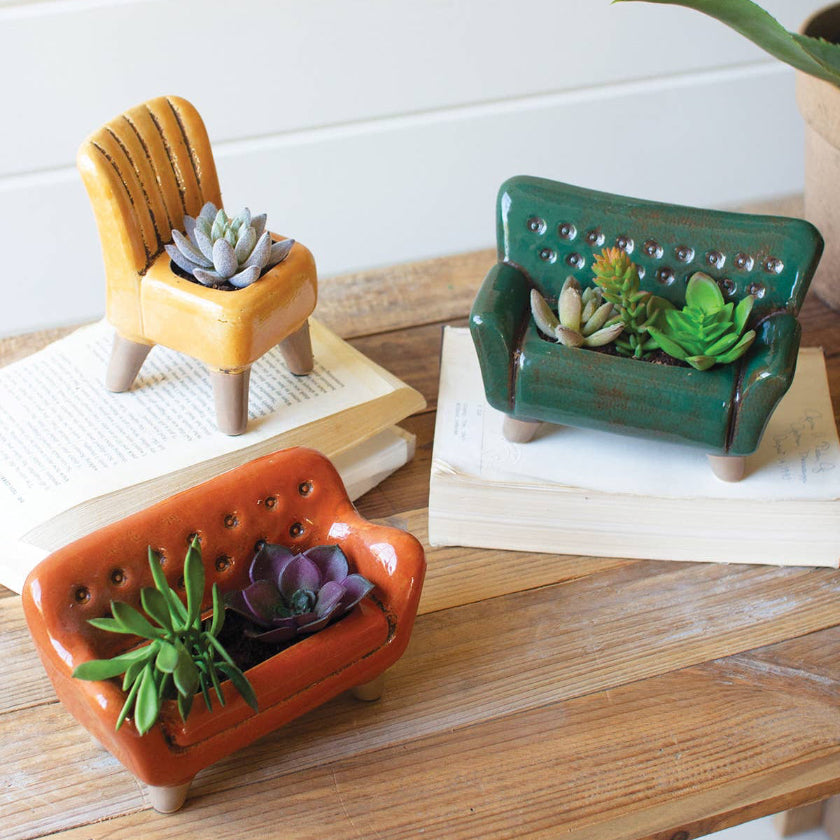 Three small ceramic planters shaped like a chair, table, and sofa with succulents on a wooden surface.