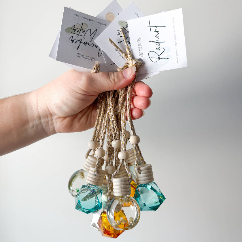 Hand holding three small glass bottles with colorful liquids and decorative elements against a plain background.