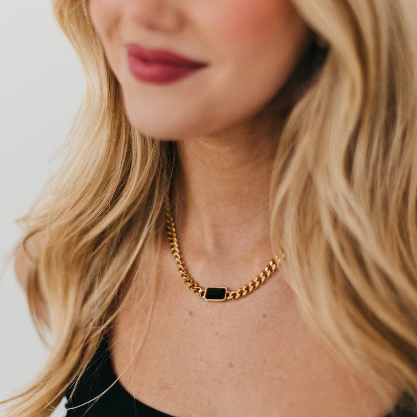 Close-up of a person wearing a gold chain necklace with a green pendant.