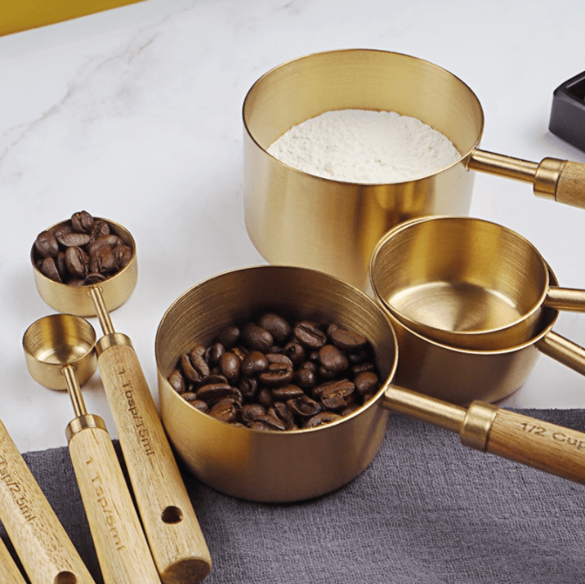 Set of brass measuring cups and spoons with coffee beans and flour on a white surface.