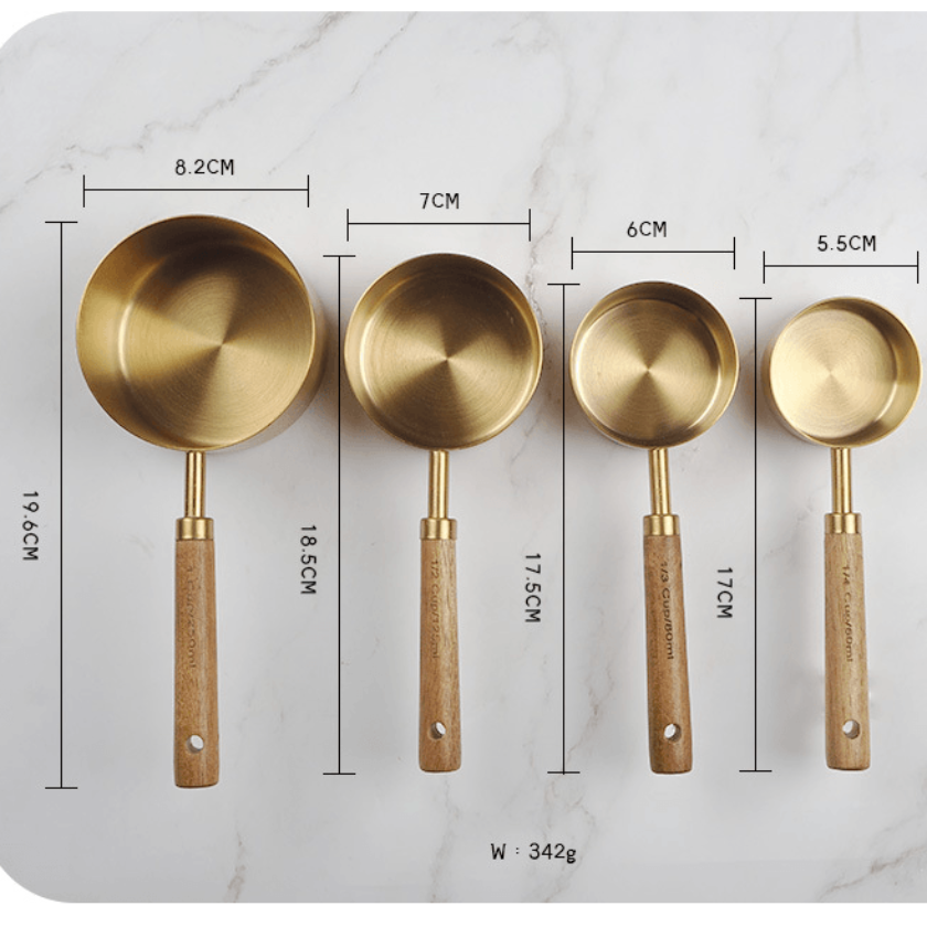 Set of four brass measuring spoons with wooden handles on a marble surface with measurements.