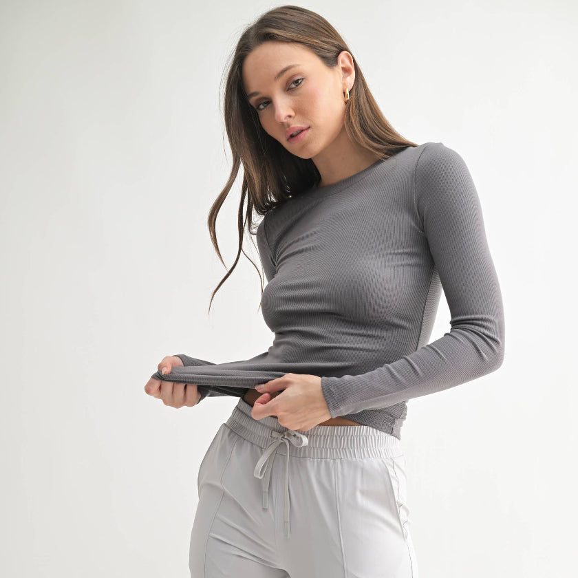 Woman wearing a gray long-sleeve top and white pants on a light gray background