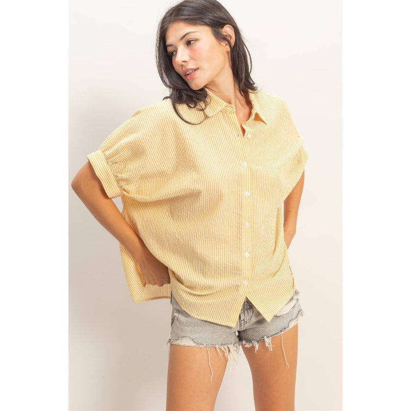 Woman wearing a yellow button-up shirt and denim shorts on a plain background