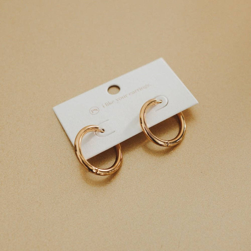 Gold hoop earrings on a white card against a beige background