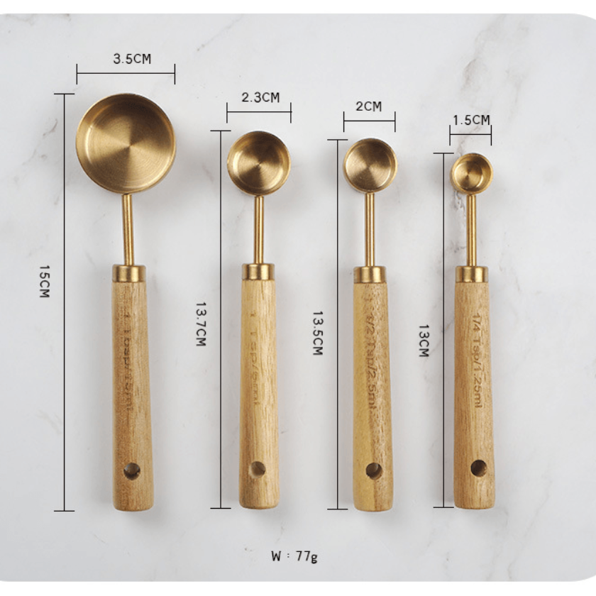 Set of four brass spoons with wooden handles on a marble surface with measurements.