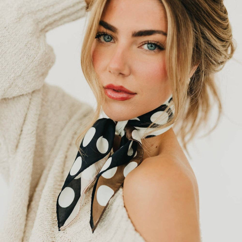 Woman wearing a black and white polka dot scarf with a neutral background
