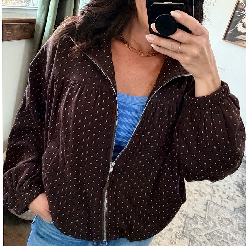 A woman takes a mirror selfie wearing a dark brown corduroy jacket with small white polka dots, layered over a blue ribbed top and jeans.