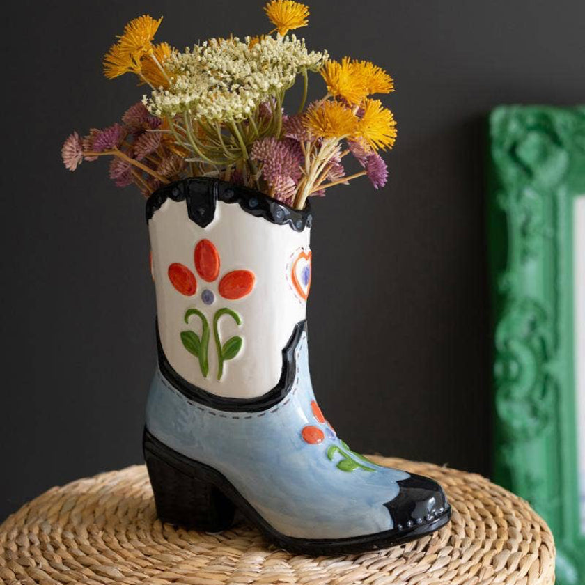 Decorative boot vase with flowers on a woven surface against a dark background