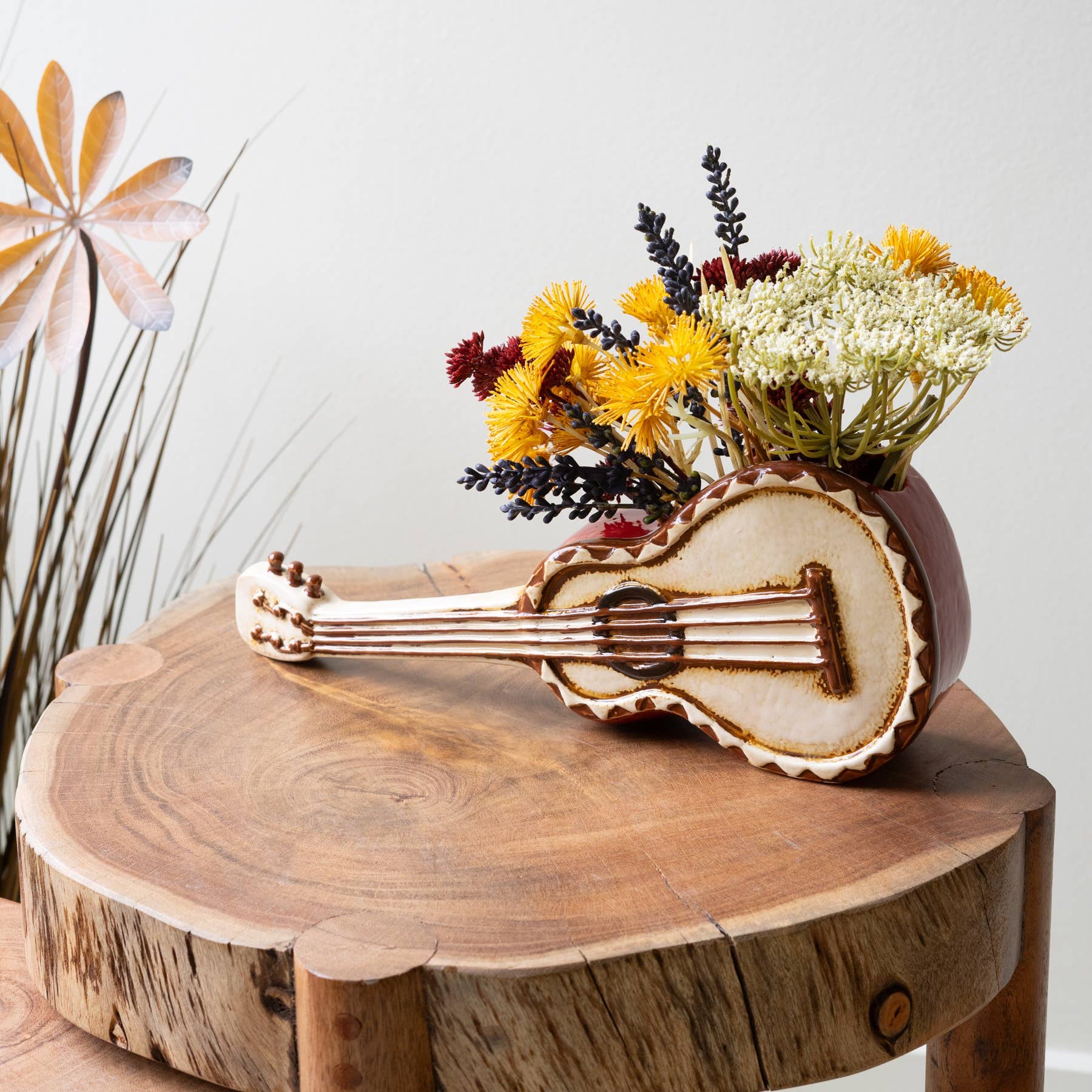 Wooden stool with a decorative vase shaped like a guitar and a small plant on a white background