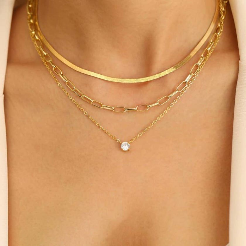 Two gold necklaces on a person's neck with a clear gemstone pendant.