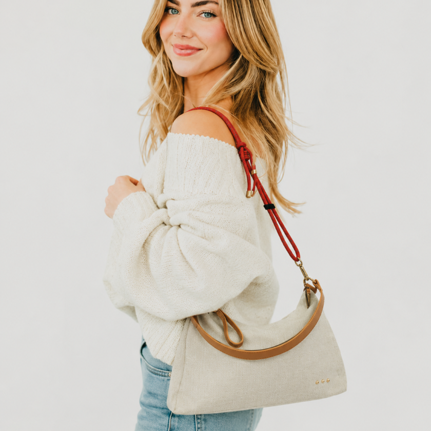 Woman holding a beige handbag with a red strap against a white background