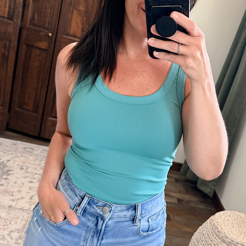 Person wearing a teal tank top and blue jeans taking a mirror selfie.