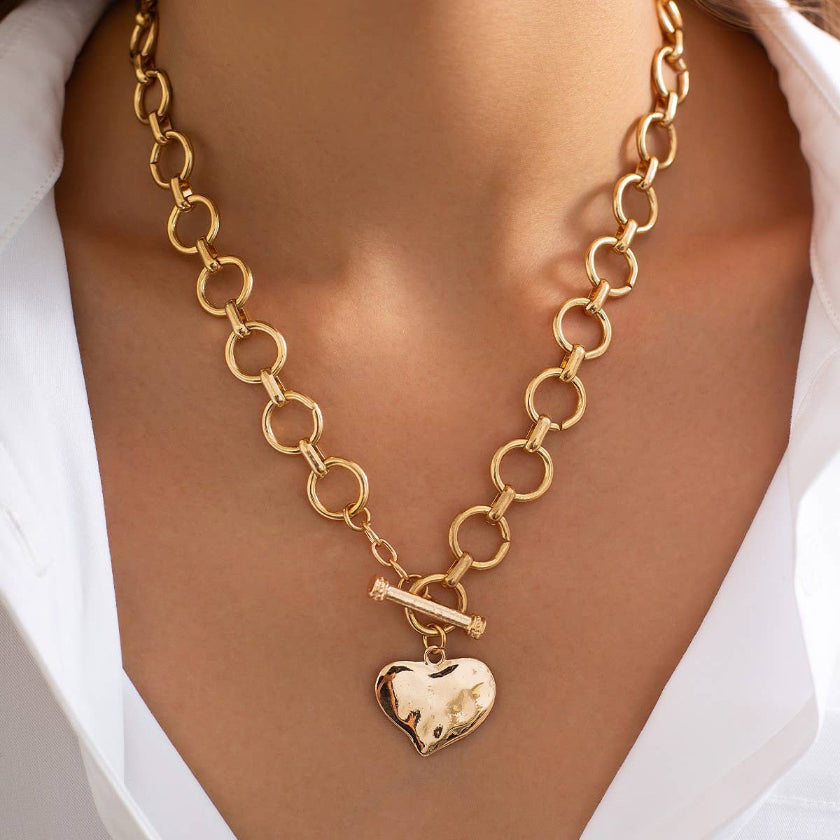 Gold chain necklace with a heart-shaped pendant on a person wearing a white shirt.