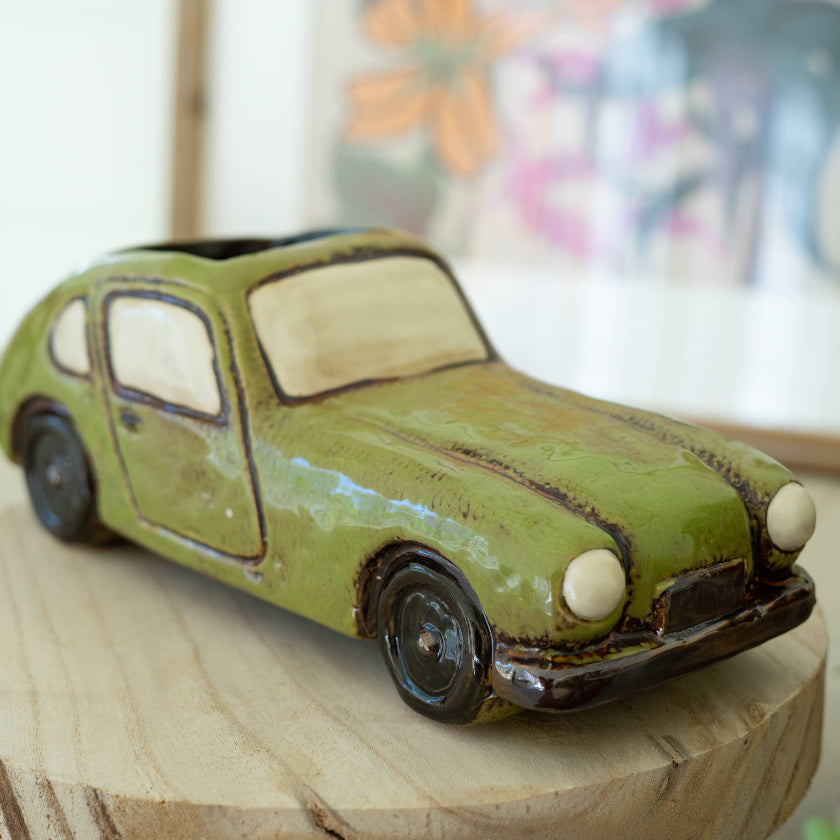 Vintage-style toy car on a wooden surface with a colorful abstract painting in the background