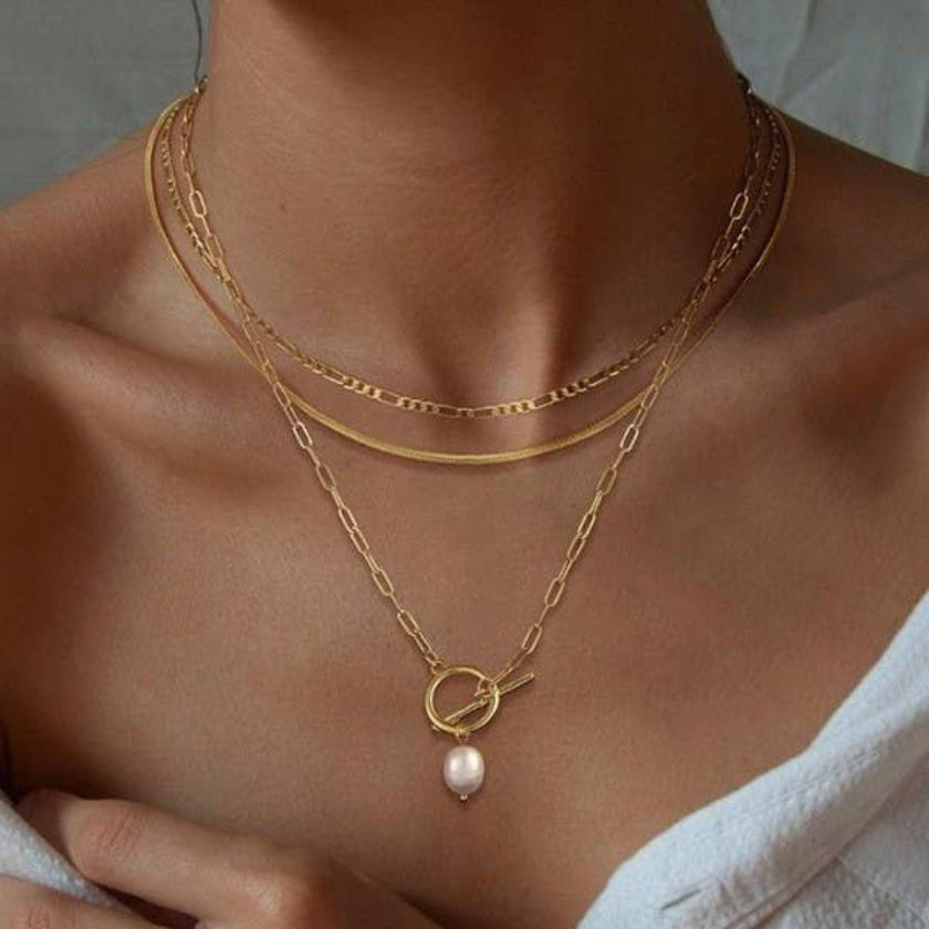 Gold necklace with a pearl pendant on a person wearing a white garment.