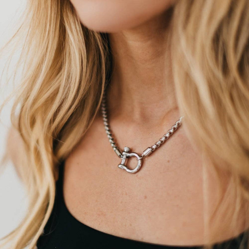 Close-up of a person wearing a silver necklace with a horse bit pendant.