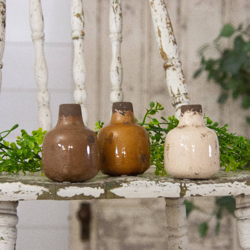 Three ceramic bottles on a rustic wooden surface with greenery in the background