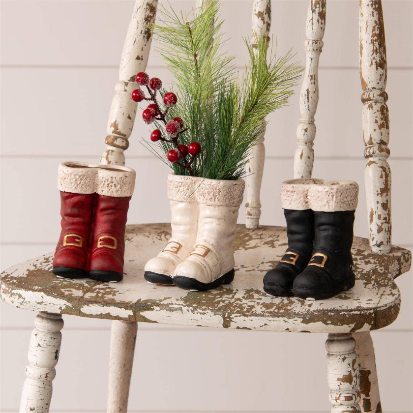 Three pairs of colorful boots on a rustic wooden chair with decorative plants.