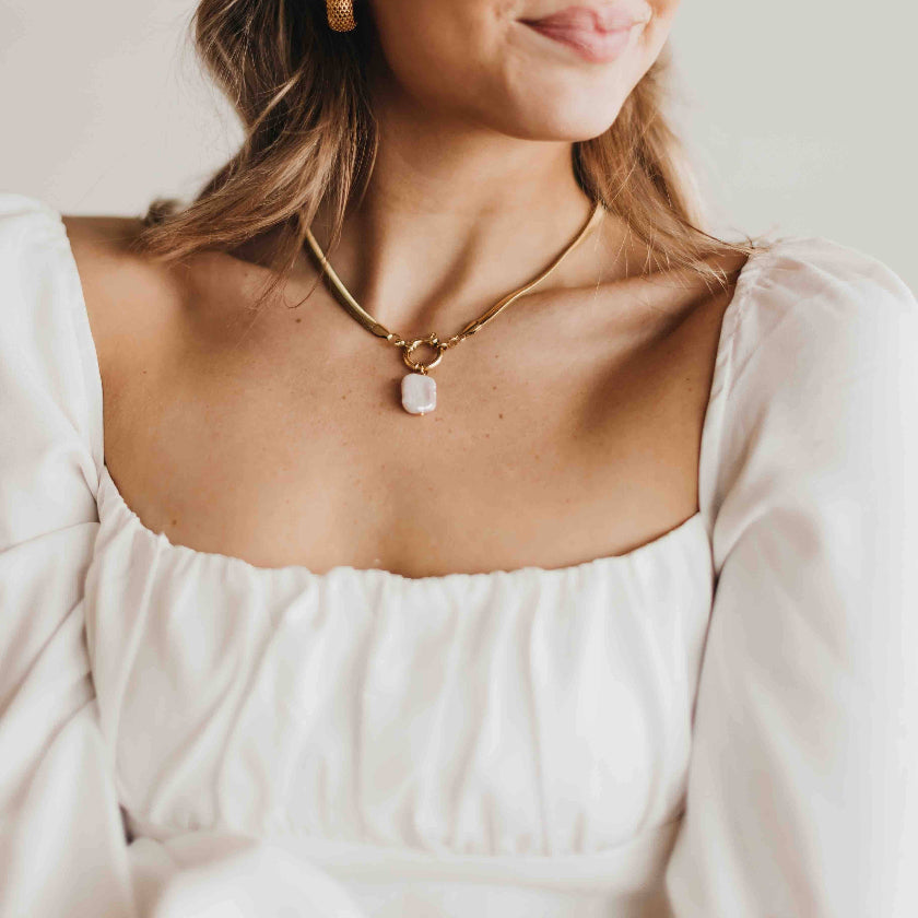 Woman wearing a gold necklace with a white pendant against a neutral background