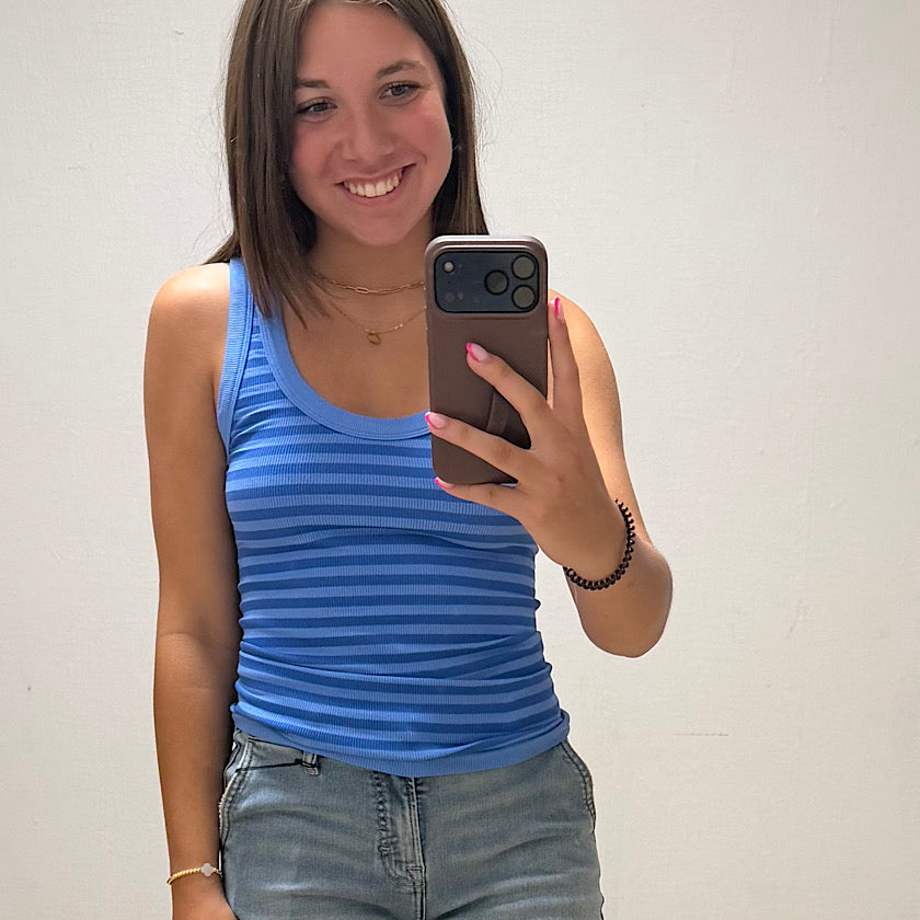 Woman taking a mirror selfie wearing a blue striped tank top and jeans.