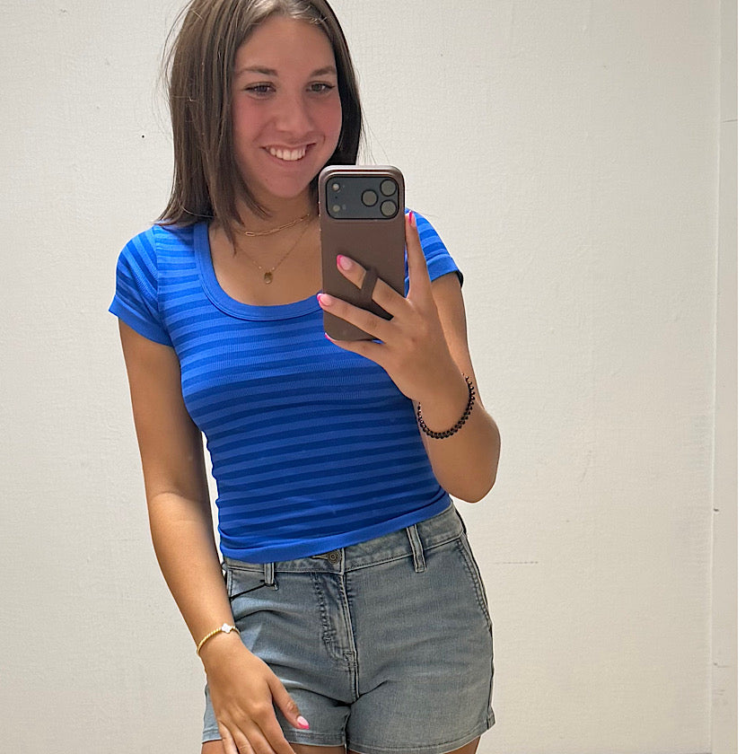 Person wearing a blue striped shirt and denim shorts taking a mirror selfie.