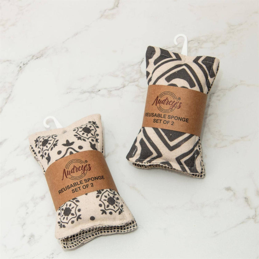 Two reusable sponge car washers by Andrey's, displayed on a white marble surface. One has a black and beige zebra print, and the other has a black and beige floral pattern, both wrapped in brown paper bands with white plastic hangers.