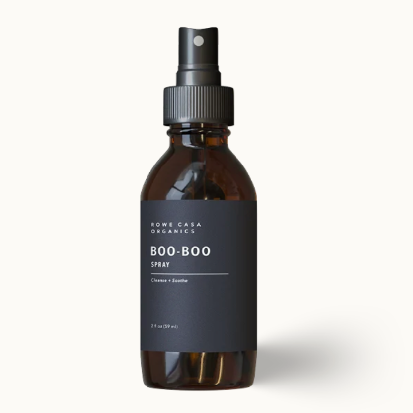 A 3 fl oz amber glass spray bottle with a black spray nozzle and a black label reading 'SOME CASA ORGANICS BOO-BOO SPRAY', centered on a clean off-white background.