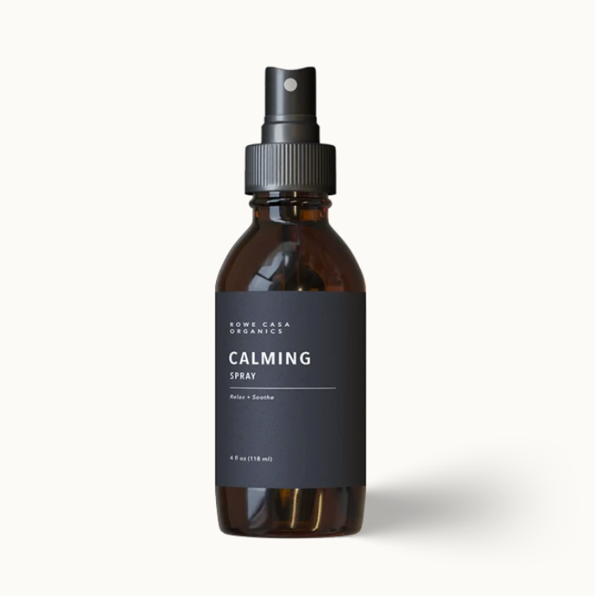 A 4 fl oz amber glass spray bottle with a black spray nozzle and a dark charcoal gray label reading 'SUNNY LAKE ORGANICS CALMING SPRAY'. The bottle is centered against a clean, off-white background with a soft drop shadow.