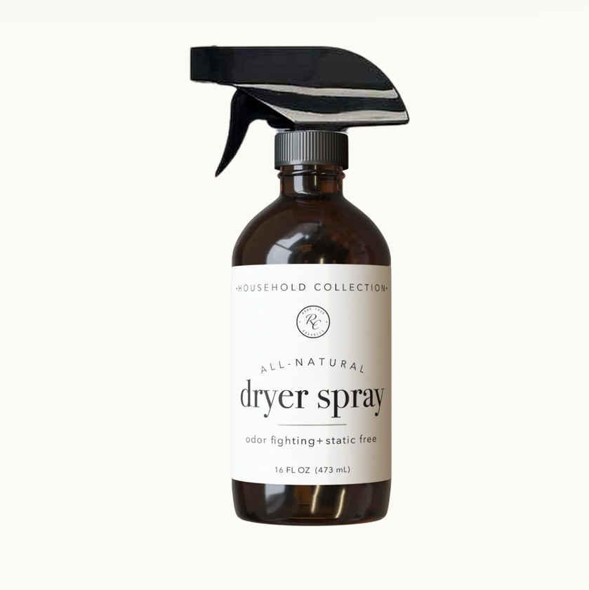 A 16 fl oz amber glass spray bottle of all-natural dryer spray with a black trigger sprayer and a white label, shown on a clean off-white background.