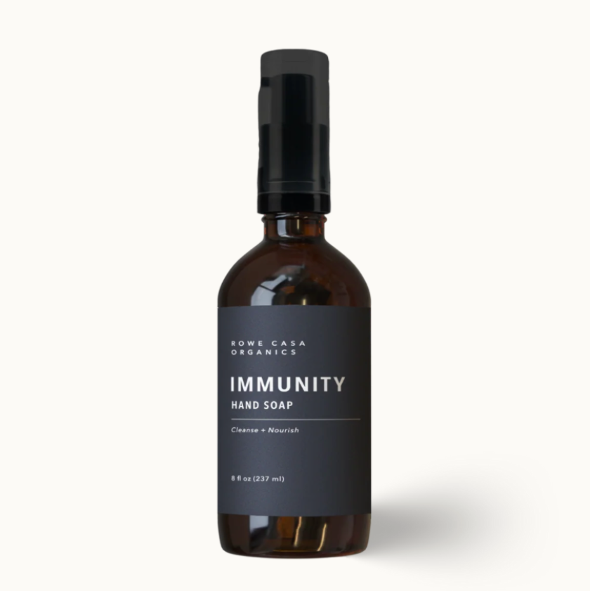 A bottle of Some Cactus Organics Immunity Hand Soap on a clean off-white background. The bottle is made of dark amber glass with a black spray cap and a dark charcoal gray label featuring white text.