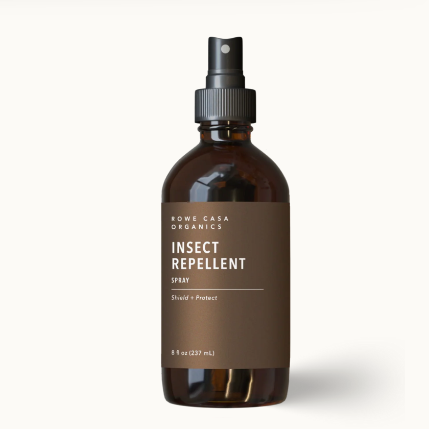 An 8 fl oz amber glass spray bottle of Rowe Casa Organics Insect Repellent Spray, featuring a dark brown label and a black spray nozzle, set against a clean off-white background with a soft shadow.