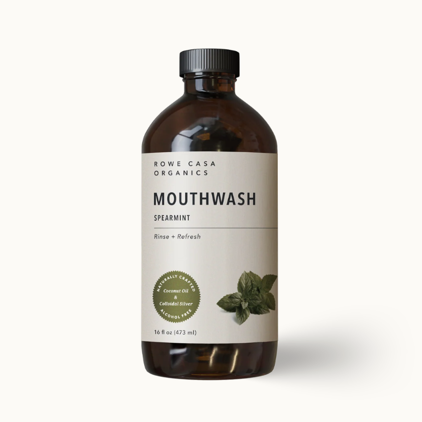 A bottle of Rowe Casa Organics Spearmint Mouthwash, featuring an amber glass bottle, a black cap, and a cream-colored label with green leaf illustrations and a green organic seal.