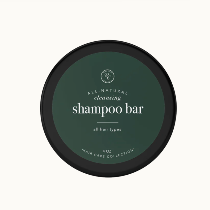 A shampoo bar packaged in a round, black container with green labeling that reads 'Rowe Casa Organics shampoo bar all hair types 4 oz'. The label also includes the text '100% natural ingredients'.