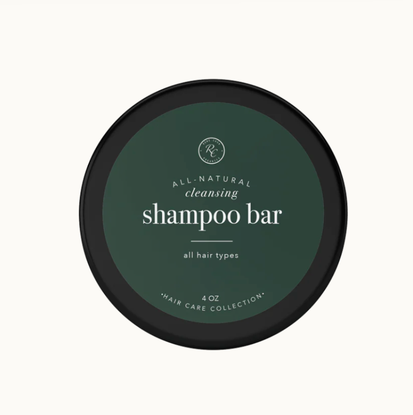 A shampoo bar packaged in a round, black container with green labeling that reads 'Rowe Casa Organics shampoo bar all hair types 4 oz'. The label also includes the text '100% natural ingredients'.