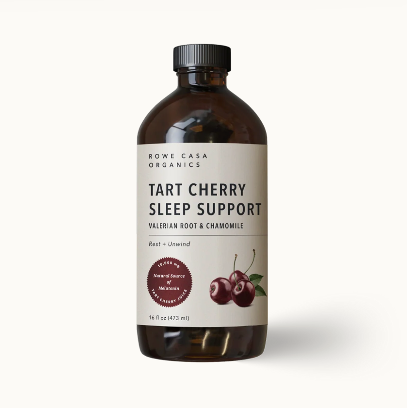 A bottle of Rowe Casa Organics Tart Cherry Sleep Support liquid supplement, featuring an amber glass bottle, black cap, and a cream-colored label with cherry illustrations, set against a plain off-white background.