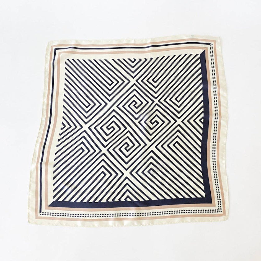 A square silk scarf featuring a black and white geometric maze pattern with a beige border, laid flat on a white background.