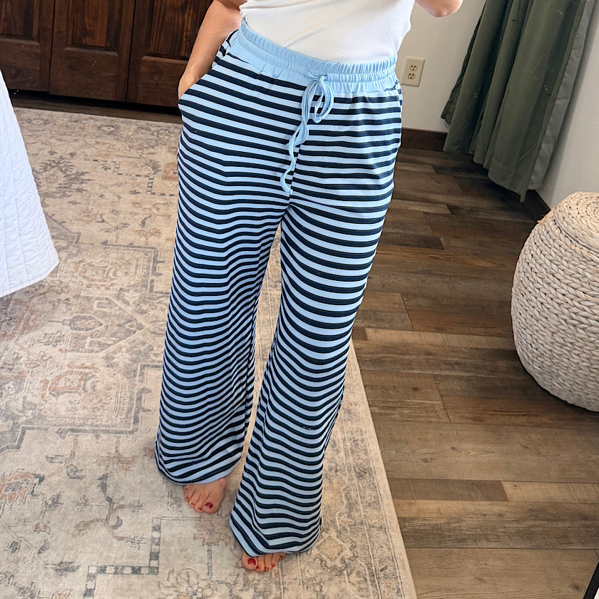 A person wearing wide-leg drawstring pants with navy and light blue horizontal stripes, standing barefoot on a patterned rug in a home interior.