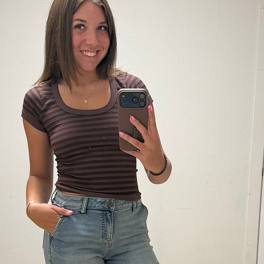 Person taking a mirror selfie wearing a brown striped shirt and blue jeans.