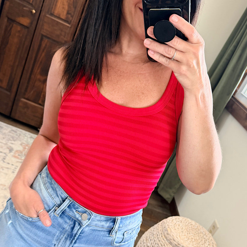 Person wearing a red tank top and blue jeans taking a mirror selfie.