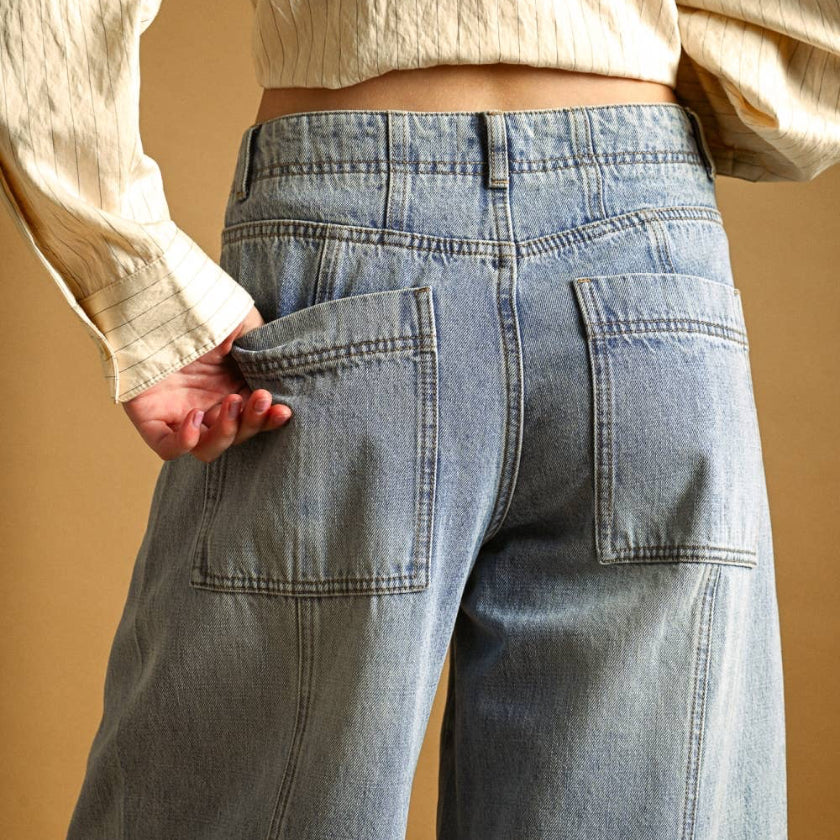 Person wearing a beige long-sleeve top and blue jeans against a beige background