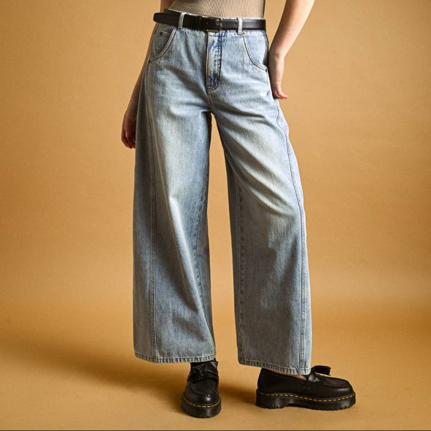 Woman wearing a beige top and light blue jeans against a beige background