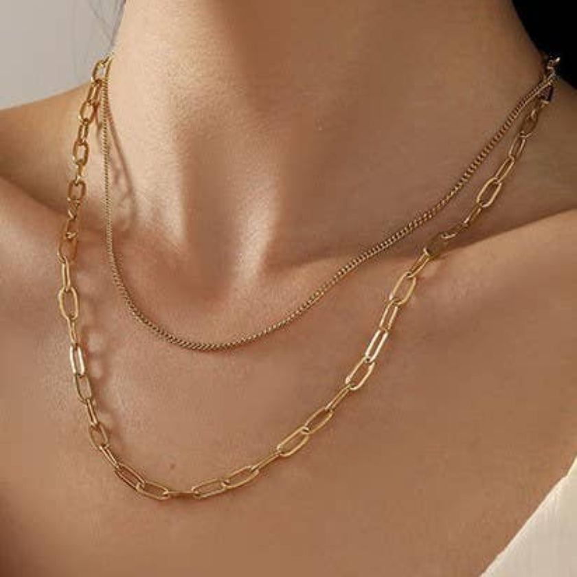 Gold chain necklace on a person's neck with a neutral background