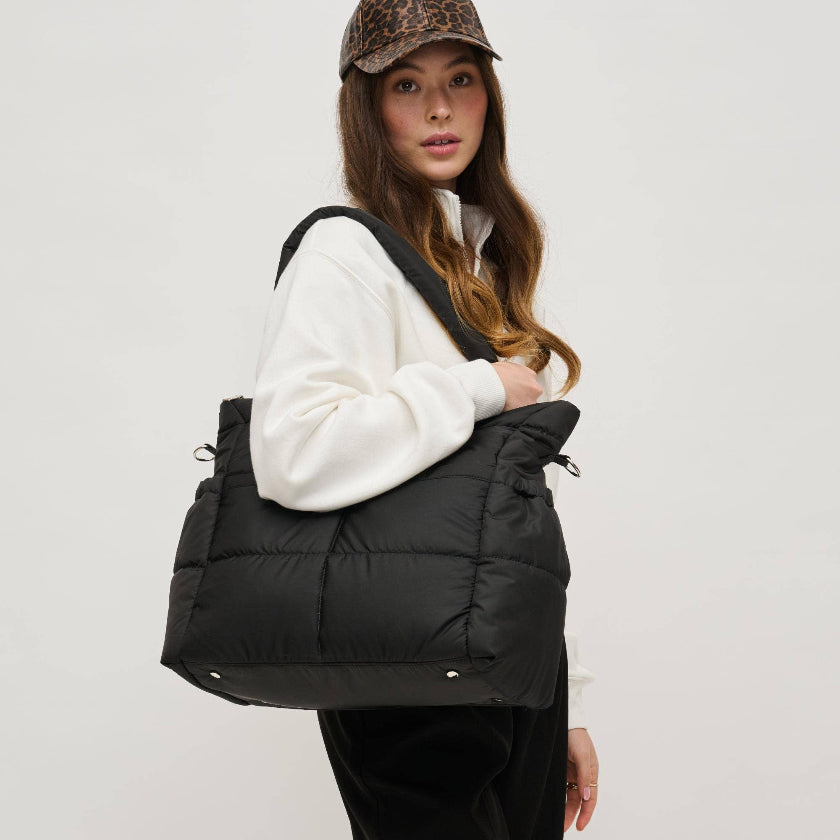 Person wearing a black puffer bag over a white jacket on a plain background