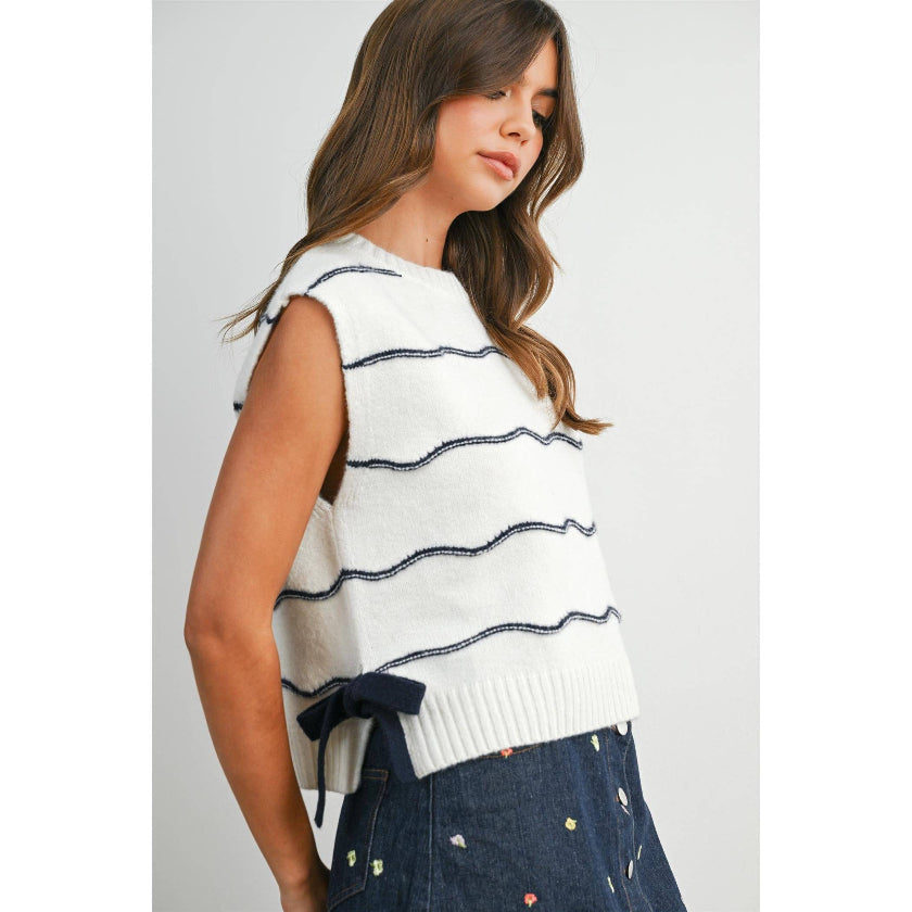 Woman wearing a white sleeveless sweater with navy stripes against a plain background