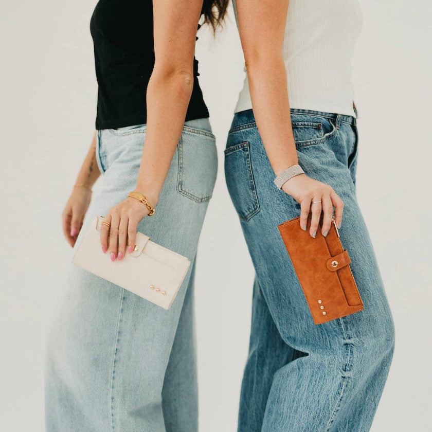 Two people wearing light blue jeans holding a beige clutch and brown wallet against a plain background.