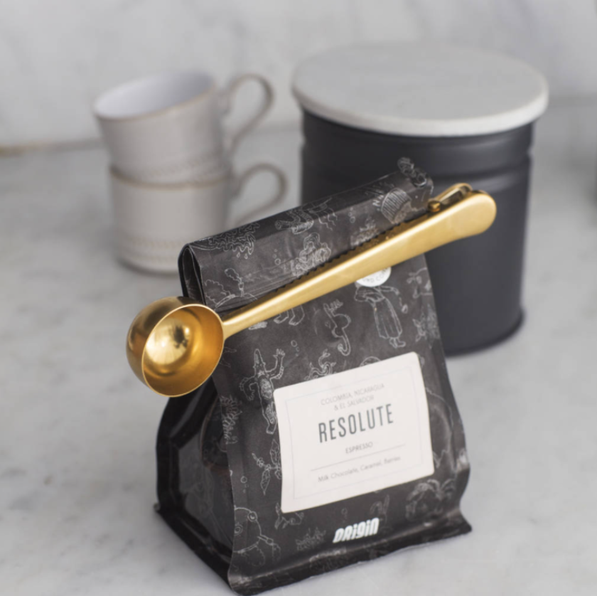 Resolute coffee bag with a gold scoop on a marble surface